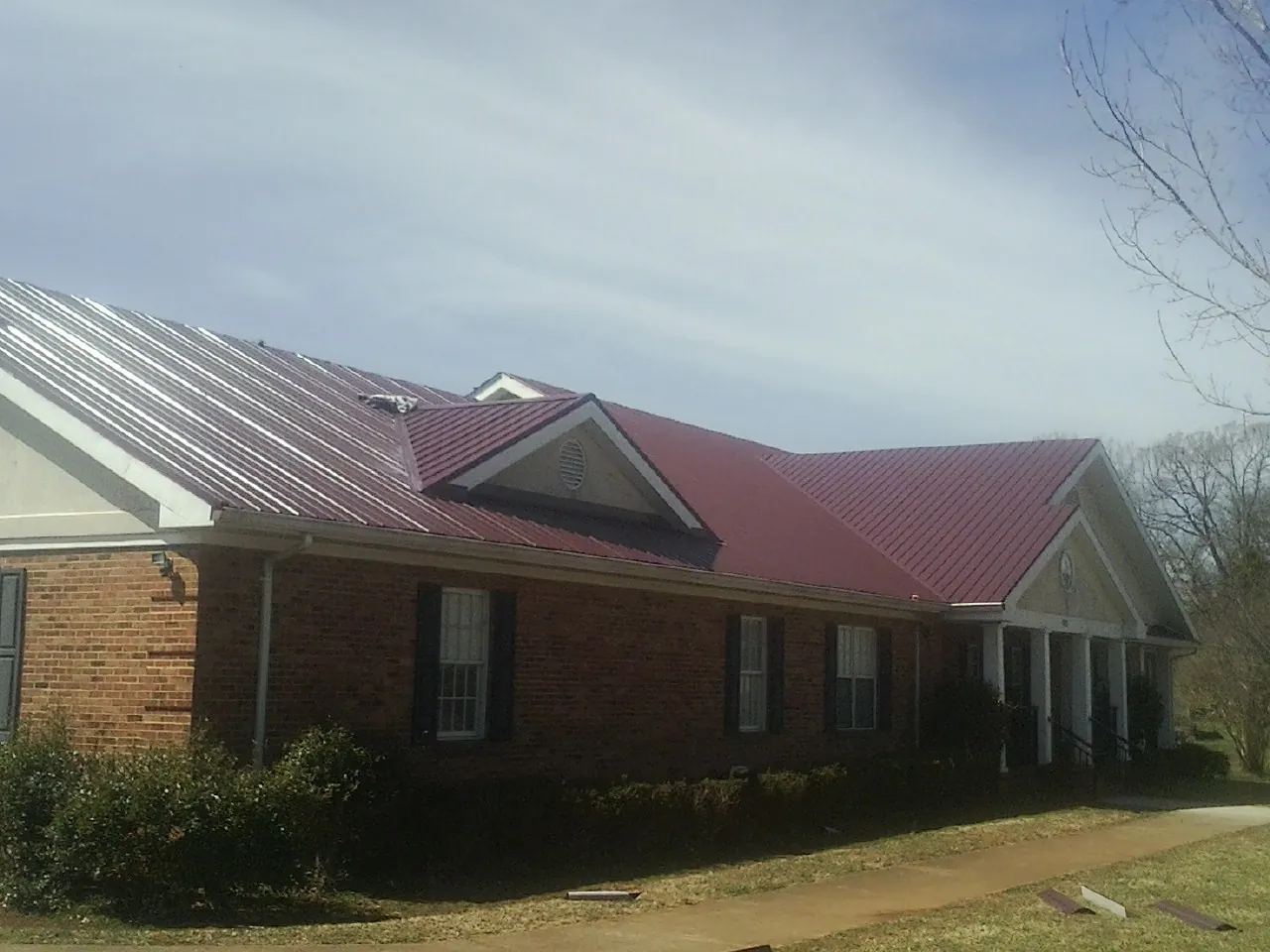 Red metal roof with gabled entries on a long brick building, from a Hail Damage Roof Repair job in Mulvane