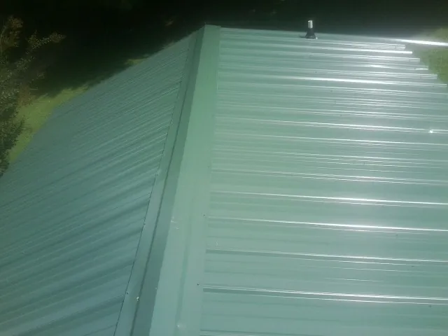 New green metal panels meeting at the ridge of a roof — Flat Roof Repair work by our crew in Mulvane
