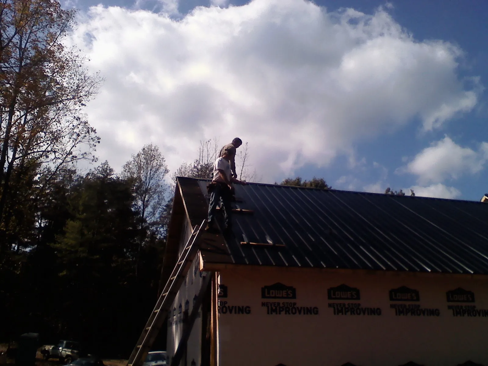 Roofer fastening dark metal panels high against a cloudy sky, from a Roof Inspection job in Mulvane